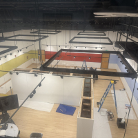 Overhead view of the Global Museum during exhibition installation, showing partially constructed gallery walls, display cases, ladders, painting supplies, and protective floor coverings
