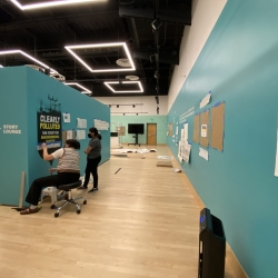 Two students apply black vinyl signace of an oil barrel onto a blue-green wall