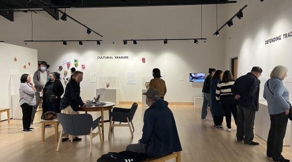 Group of adults of all ages talk and view objects in a museum gallery